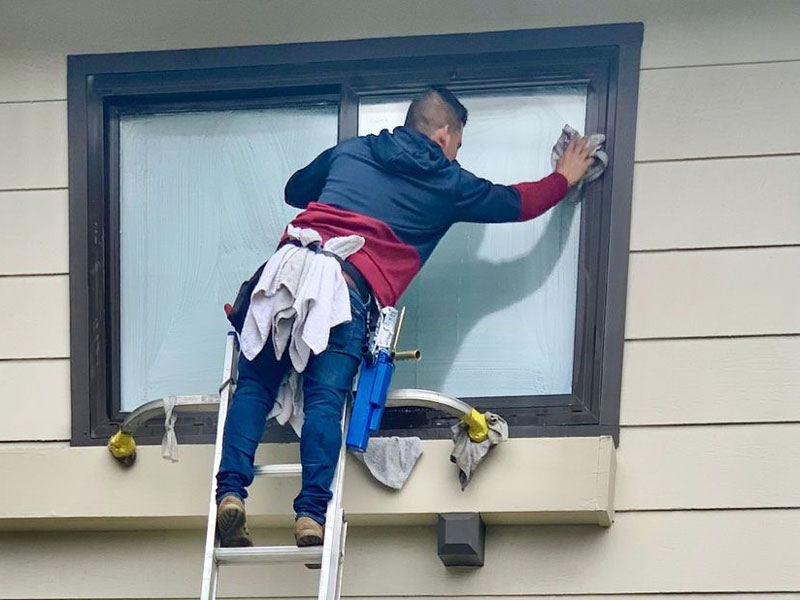 man on ladder cleaning outside of window